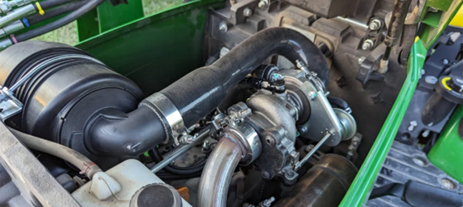A turbocharger installed in the engine bay of a modern green tractor, showing the connected hoses and pipes.