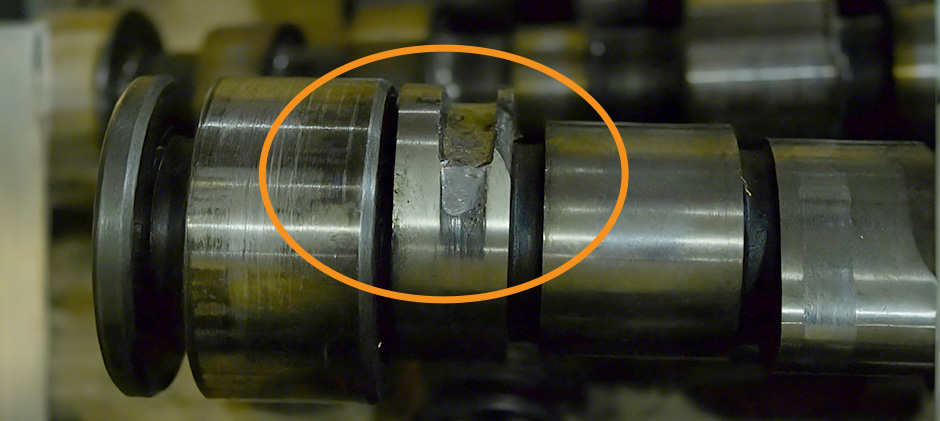 An orange circle highlights a severely damaged camshaft lobe with a large chunk of metal missing, which is typically unrepairable.