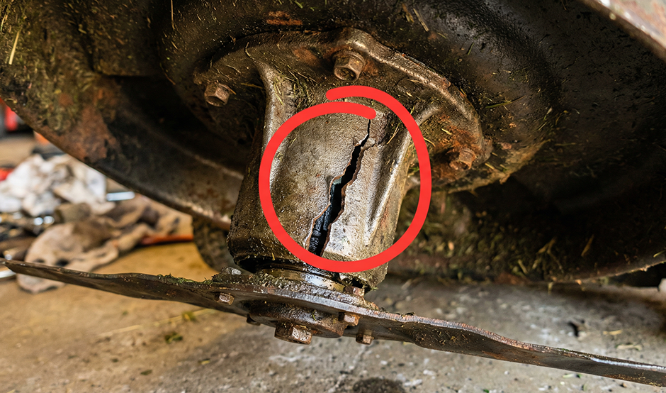 A close-up view of a cracked mower deck spindle, showing severe damage that indicates it needs to be replaced.