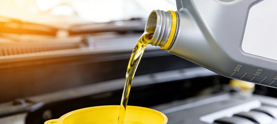 Pouring clean, amber-colored engine oil from a container into a funnel in an engine bay.