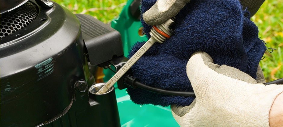A close-up of a person in gloves checking the lawn mower's oil level with a dipstick, a key step in diagnosing engine issues.