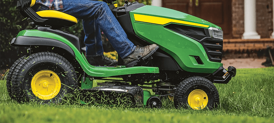 Close-up of a John Deere lawn tractor in action, cutting grass on a residential lawn.