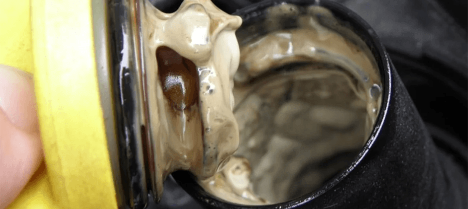 Close-up of a milky, coffee-colored sludge on an engine oil filler cap, a clear sign of coolant mixed with oil.