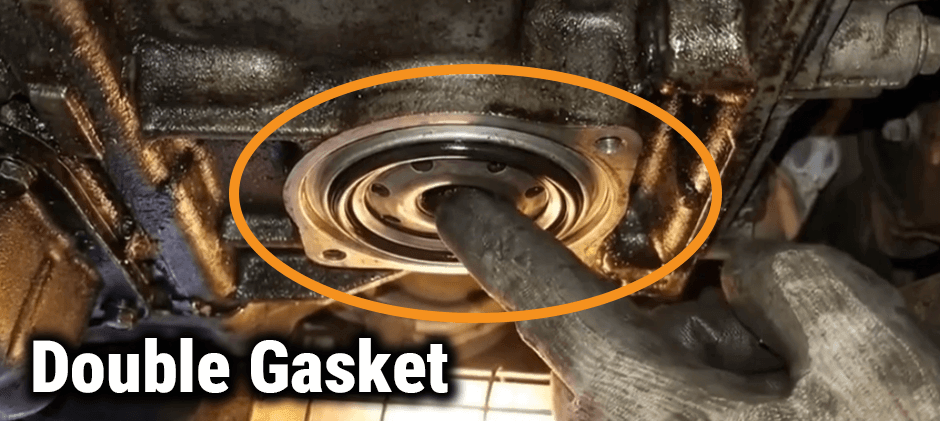 A mechanic's finger pointing to an old oil filter gasket stuck on the engine block, a common cause of a double gasket oil leak.
