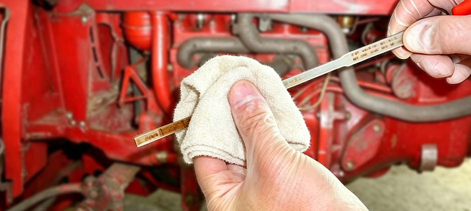A technician in gloves inspects the oil level on a dipstick from a red heavy-duty diesel engine.