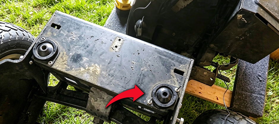  The underside of a machine showing two new, black engine mounts bolted to the frame, with a red arrow pointing to one. Learn bad engine mount symptoms.