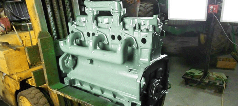 A fully rebuilt heavy-duty engine painted green, being moved by a forklift in a repair shop.
