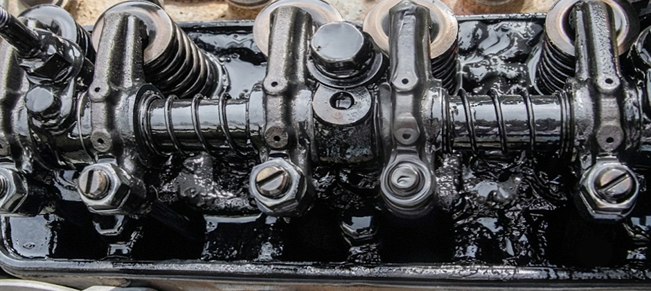 The valvetrain of a diesel engine, including rocker arms and valve springs, completely covered in sticky, black oil sludge.