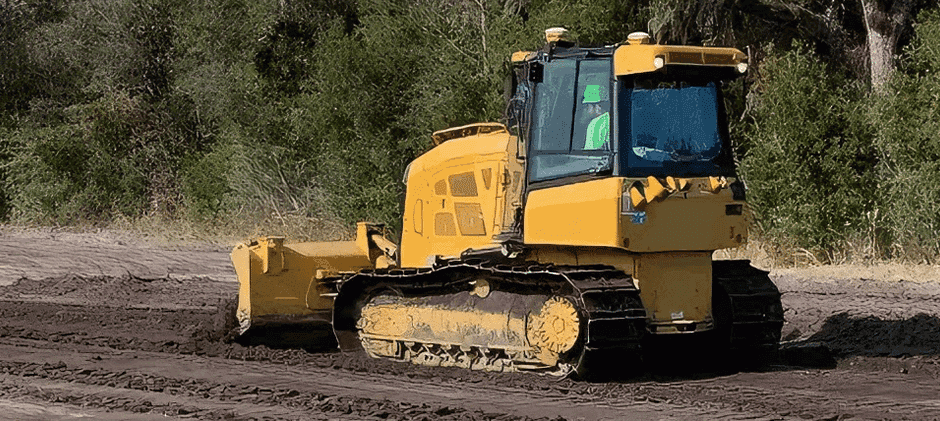 A yellow bulldozer with its tracks deep in mud, grading the ground and showcasing the need for steady torque to avoid getting stuck.