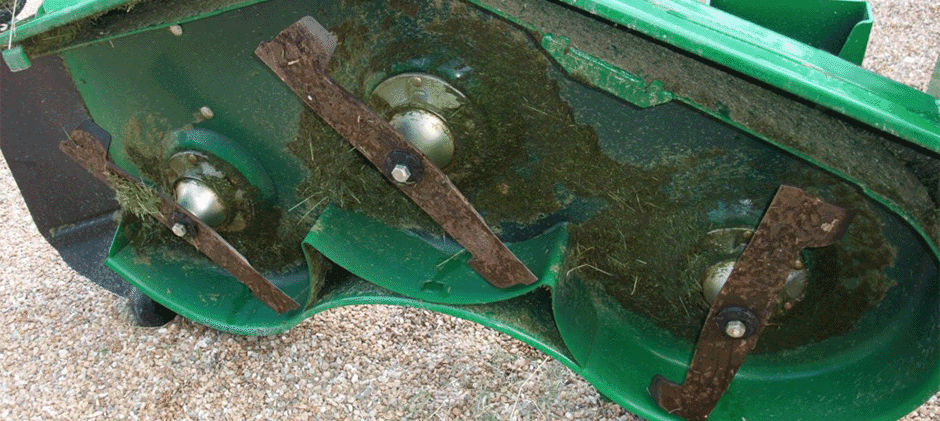 Close-up of three dirty mower blades under a deck after cutting grass, showing how they do not stay aligned during normal operation.