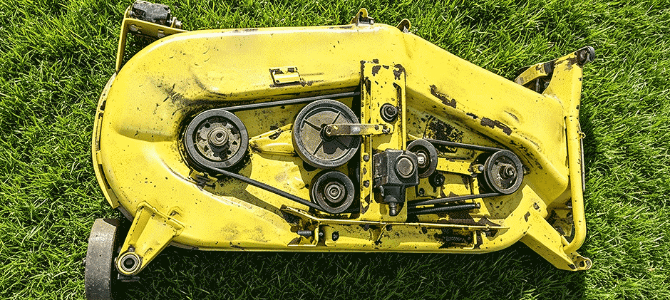  Top-down view of a used yellow mower deck showing the worn drive belt and pulley system ready for inspection and repair.