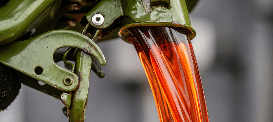 A close-up of red dyed off-road diesel being poured from a fuel nozzle into the tank of a piece of heavy equipment.