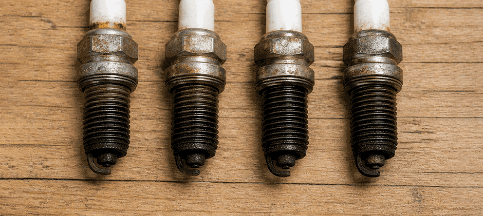 Four used spark plugs lined up, showing oil and grime on the threads while the firing tips remain relatively clean.