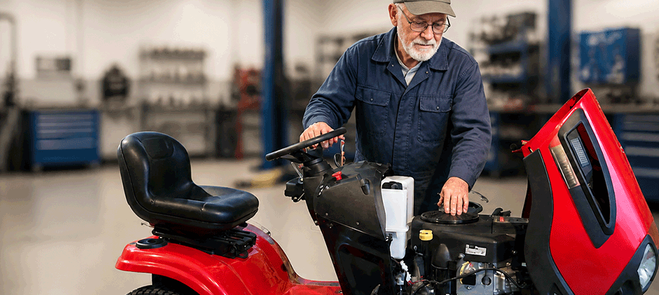 A man leans over a red riding lawn mower with the hood open, inspecting the engine area to diagnose why the machine won't start.