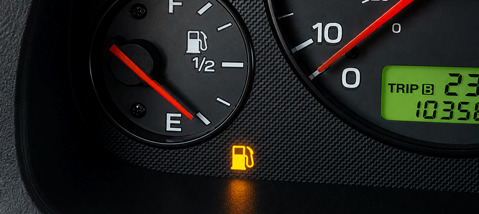 A car's fuel gauge showing an empty tank with the orange low fuel warning light turned on.
