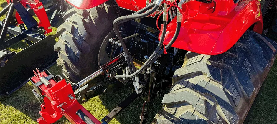 La parte trasera de un tractor rojo muestra los cilindros y las mangueras hidráulicas conectados a un implemento del enganche de tres puntos.