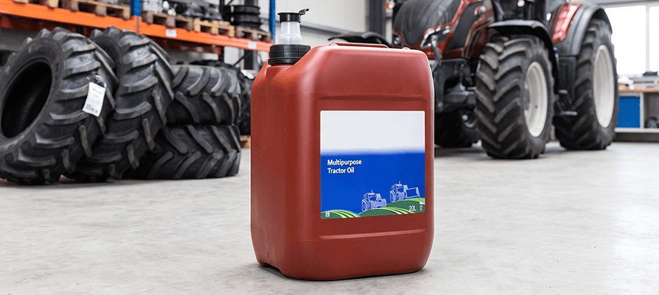 A red jug of multipurpose tractor oil sitting on a workshop floor in front of a tractor. JDM J20C equivalent