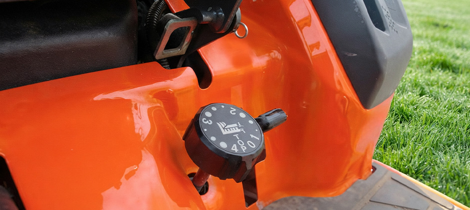 Close-up view of the black height adjustment knob on the orange fender of a Kubota mower, showing numbered settings.