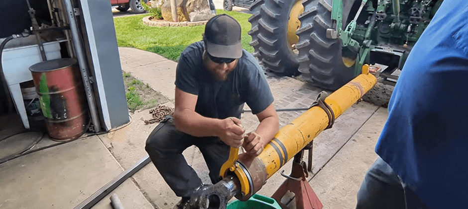 Technician at a workbench removing a hydraulic cylinder gland while the cylinder is securely supported.