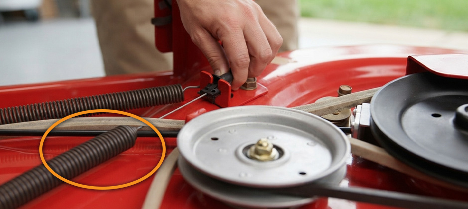 Close-up of the PTO cable spring highlighted in an orange circle on a Troy-Bilt mower deck.