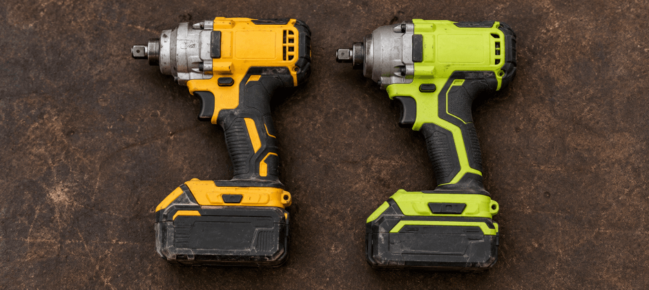 Top view of heavily used DeWalt and Ryobi impact drivers resting on a shop floor.