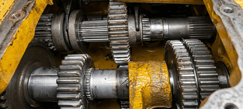 Heavy equipment transmission internals showing gears, splined shafts, and shift forks inside a yellow housing.